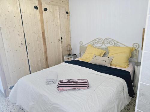 a white bed with yellow pillows and a towel on it at La brise marine - proche de la mer in Valras-Plage