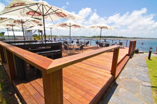 a wooden deck with tables and umbrellas on the water at Comfort Resort Waters Edge in Port Macquarie