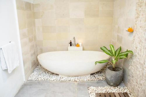 La salle de bains est pourvue d'une baignoire blanche et d'une plante en pot. dans l'établissement Villa Pagu, à Seminyak