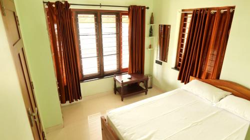a bedroom with a bed and two windows and a table at Atharvam Resort in Cherai Beach