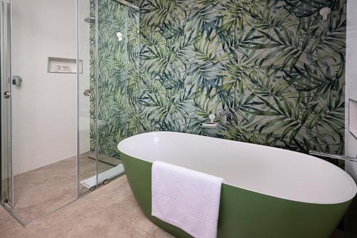 a bath tub in a bathroom with a green leaf wallpaper at Topiary Lux Studio 16! in Herolds Bay