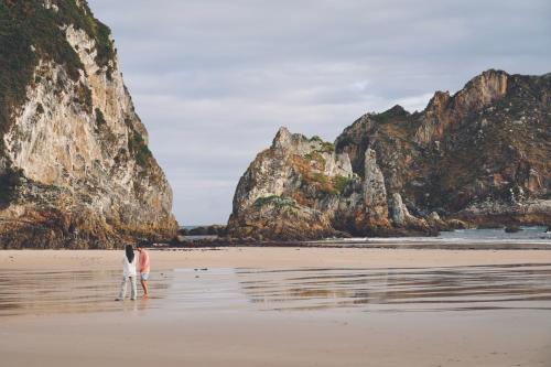 a couple walking on a beach with cliffs at HolaCamp la Franca in Las Conchas