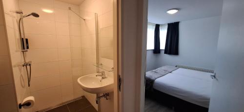 ein Badezimmer mit Waschbecken und Dusche sowie ein Bett in der Unterkunft Seehotel Oostkapelle in Oostkapelle