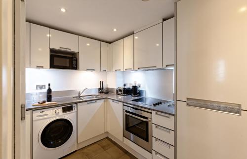 a kitchen with white cabinets and a washer and dryer at Oxford Street Fitzrovia Apartments by DMONTRIO in London