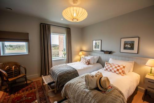 a bedroom with two beds and a chair and a window at The Barn at Manor Farm in Great Glemham