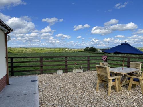 a patio with a table and chairs and an umbrella at Sunny Bank - bungalow with hot tub and extra accessibility in Carmarthen