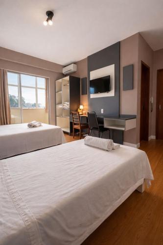 a hotel room with two beds and a desk at Hotel Nossa Casa in Ijuí