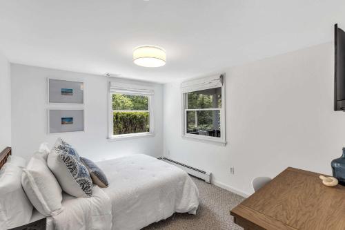 a white bedroom with a bed and two windows at Jenkins Pond Beach Access with BBall Hoop & Grill, Bright Cape Cod Retreat near Jenkins Pond in Falmouth - Parking, Modern Retreat with Outdoor Space, 24 Hour Hospitality in Falmouth