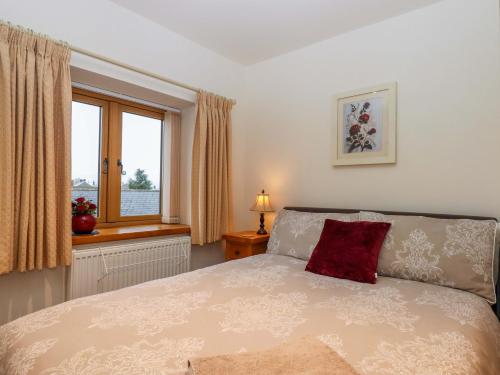 a bedroom with a bed with a red pillow and a window at Grange Cottage in Crediton