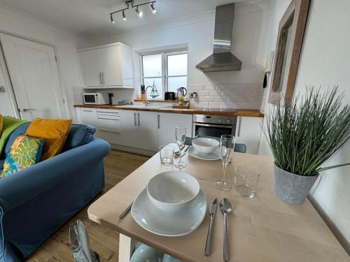 a kitchen with a table with plates and glasses on it at AnchorageWells Harbour Apartment in Wells next the Sea