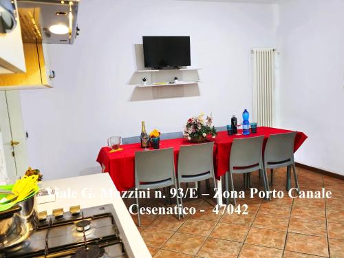 a kitchen with a red table with chairs and a tv at Appartamenti Cangini in Cesenatico