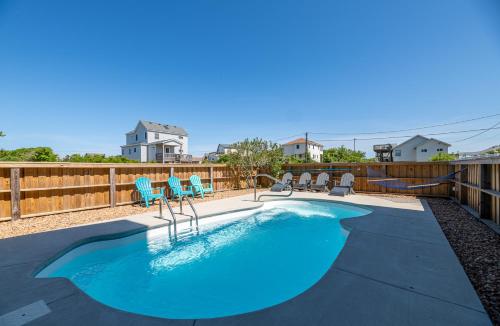 a swimming pool with blue chairs and a fence at Carolina Cottage - Kitty Hawk, Oceanside, Walk to Beach, Pool, Hot Tub, Pool Table in Kitty Hawk