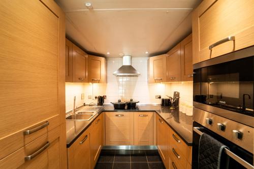 a kitchen with wooden cabinets and black appliances at Cozy 2BR Apt in Greenwich, Near O2 Arena and Excel, Fast Wi-Fi, Free Parking, Excellent links Elizabeth and Southeastern Line in London