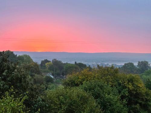a sunset over the hills with trees in the foreground at Hillside Hideaway in Flaxley