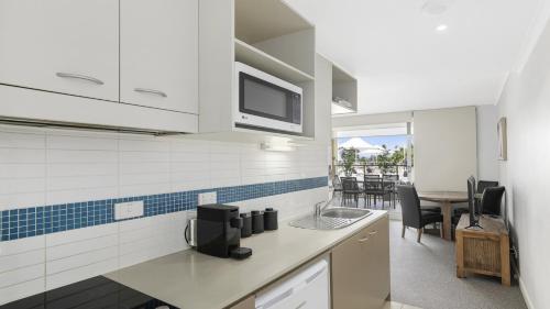 a kitchen with white cabinets and a table with chairs at Poolside Paradise Ettalong Beach Resort in Ettalong Beach