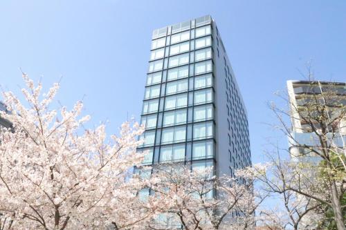 a tall glass building withakura trees in front of it at Hotel Keihan Tsukiji Ginza Grande in Tokyo