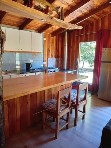 a kitchen with a large wooden counter with two chairs at Cabaña borde rio in Pucón