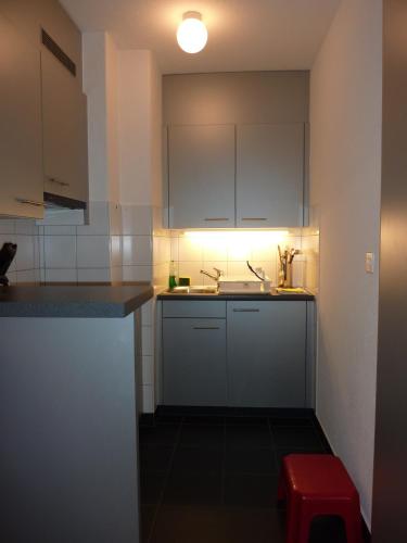 a kitchen with white cabinets and a red stool at Appartements Hofquartier in Luzern