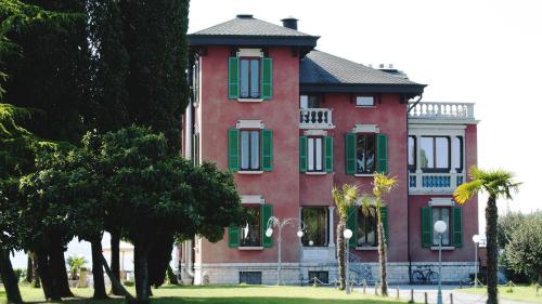 um grande edifício vermelho com persianas verdes e árvores em Villa Pioppi Hotel em Sirmione