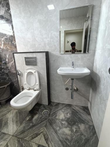 a man taking a picture of a bathroom with a toilet and sink at Sathya Comforts in Bangalore