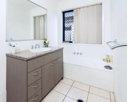 a bathroom with a sink and a tub and a mirror at House 4-bed 2-bath Caboolture South in Caboolture