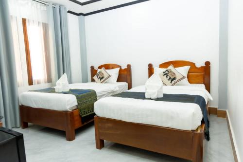a bedroom with two beds with white sheets and a tv at Oudomsin Guesthouse in Luang Prabang