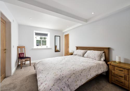 a white bedroom with a bed and a chair at The Studio at Pitmeadow Farm in Dunning