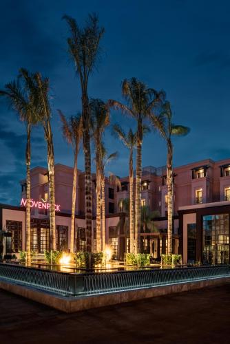 a hotel with palm trees in front of a building at Mövenpick Hotel Mansour Eddahbi Marrakech in Marrakech