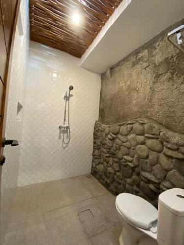 a bathroom with a toilet and a stone wall at Dava Guest House Gianyar in Gianyar