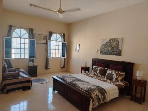 a bedroom with a bed and a chair and windows at Bustan Shells House in Muscat