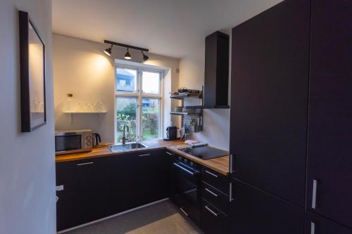 a kitchen with black cabinets and a sink and a window at Odinsvej Apartments - by Central Lyngby Apartments in Kongens Lyngby