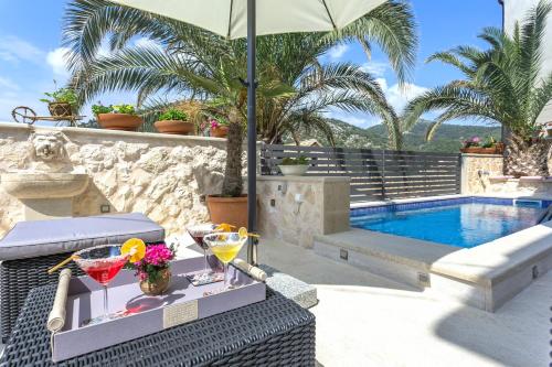 a table with drinks and an umbrella next to a swimming pool at Villa Capitis in the Centre - Private Pool Villa & Balcony Apartment with Spectacular View-No Pool in Hvar