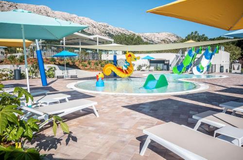 a pool with a playground with tables and umbrellas at Camping Baska in Krk