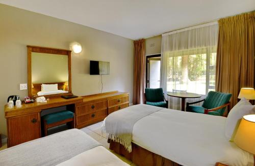 a hotel room with two beds and a desk and a mirror at Pilanesberg Hotel in Boshoek