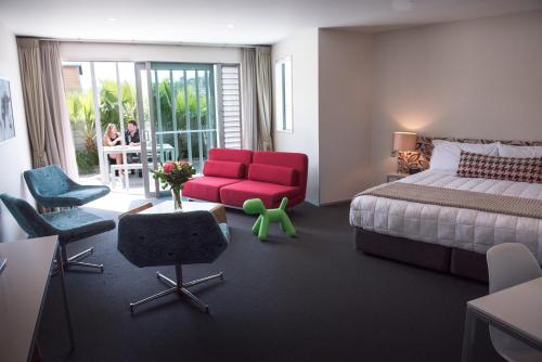 une chambre d'hôtel avec un lit et un fauteuil rouge dans l'établissement Navigate Seaside Hotel & Apartments, à Napier
