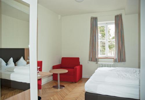 a hotel room with two beds and a red chair at Hotel Landgut Burg in Weinstadt