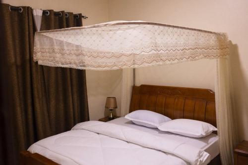 a bedroom with a canopy bed with white sheets and pillows at Green Hill Stay in Fort Portal