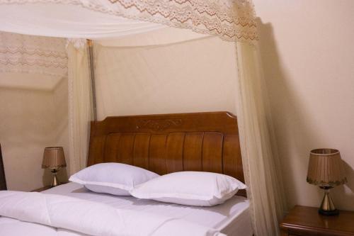 a bed with a wooden headboard and white pillows at Green Hill Stay in Fort Portal