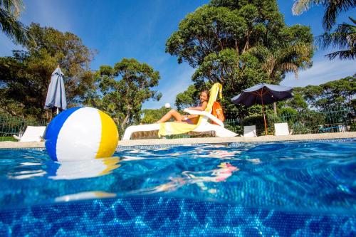 a woman sitting in a chair next to a swimming pool at NRMA Broulee Holiday park in Broulee