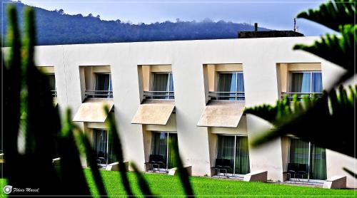 a white building with windows and a mountain in the background at Pousada de Angra do Heroismo Castelo de S. Sebastiao in Angra do Heroísmo