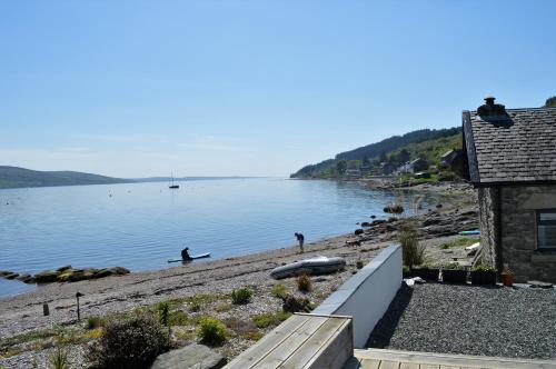 a beach with a house and people on the water at Pier Cottage at Kames in Kames
