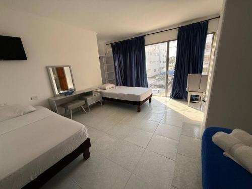 a bedroom with two beds and a desk and a window at Hotel Toledo FL in Cartagena de Indias
