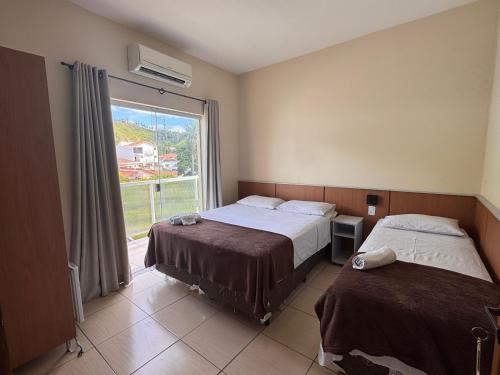 a hotel room with two beds and a window at Pousada Santa Gianna in Aparecida