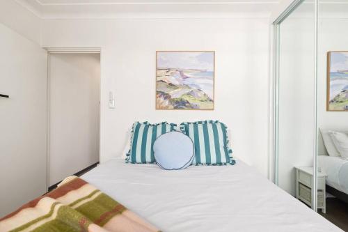 a white bedroom with a bed with striped pillows at Shoreleaf Haven - Moments from Waves & Seaside Eats in Deewhy