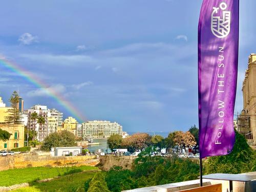 a purple banner with a rainbow in the background at Follow the Sun Boutique Hostel - Pool, Breakfast & Sea Views in St. Julianʼs