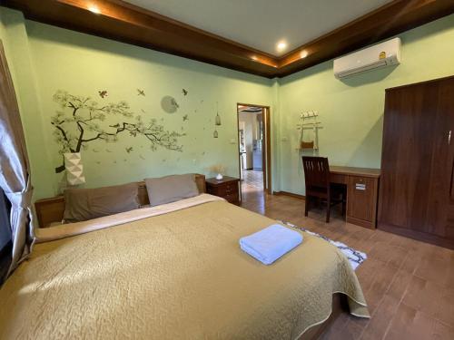a bedroom with a large bed with a desk and a tree on the wall at Srisook House in Ko Phangan