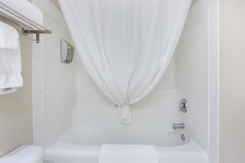 a white bathroom with a tub and a shower curtain at Lakeview Inns & Suites - Okotoks in Okotoks