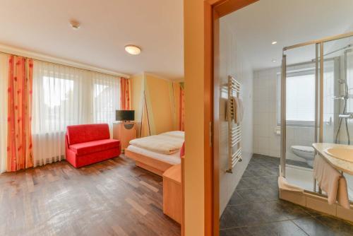 a bathroom with a bedroom with a bed and a red chair at Hotel Peterhof in Dietenheim
