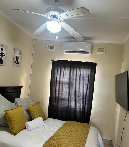 a bedroom with a ceiling fan and a bed with yellow pillows at Dube Villa in KwaDukuza