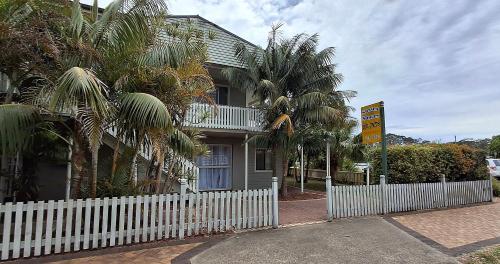 a white fence in front of a house with palm trees at Sussex Shores in Sussex inlet